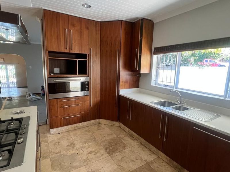 A functional kitchen featuring warm-toned wooden cabinetry, stone countertops, a gas hob, and a stainless steel double sink with natural light.