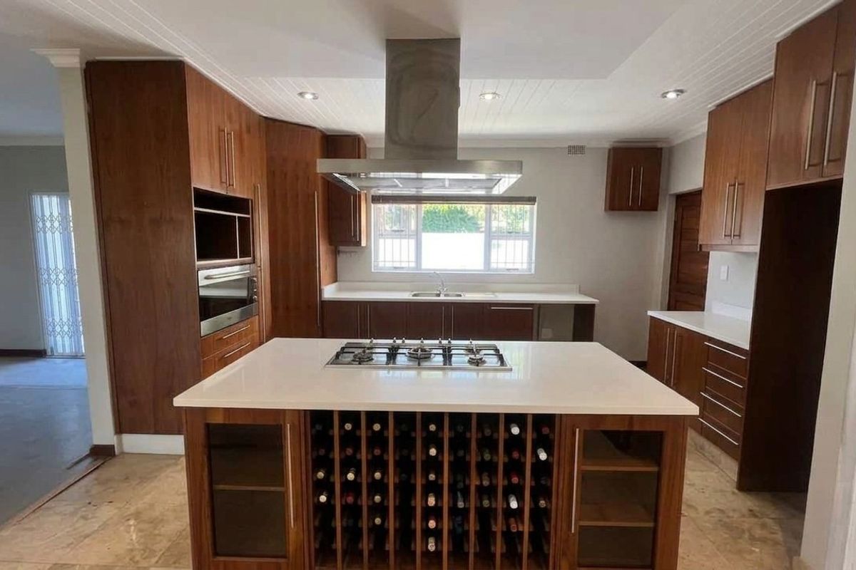 Spacious kitchen featuring a central island with a built-in gas hob, wine storage, stone countertops, and ample wooden cabinetry with integrated appliances.