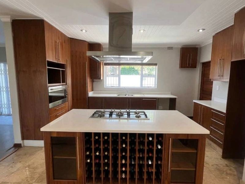 Spacious kitchen featuring a central island with a built-in gas hob, wine storage, stone countertops, and ample wooden cabinetry with integrated appliances.