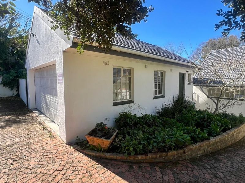Exterior view of a detached garage with a tiled roof, white rendered walls, and a brick-paved driveway with a landscaped garden bed.