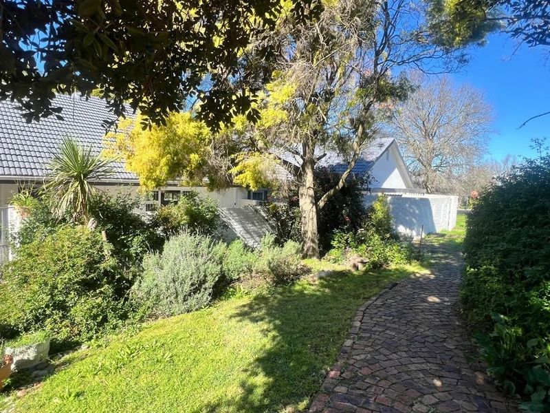 A lush garden area featuring a winding cobblestone pathway leading towards the side of the house with a tiled roof.
