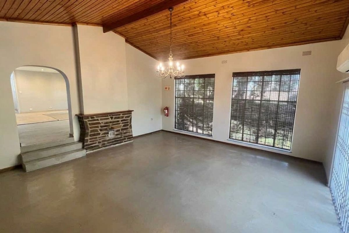 Spacious living room featuring a stone fireplace, vaulted timber ceiling, polished concrete floors, and direct access to the exterior via a security gate.