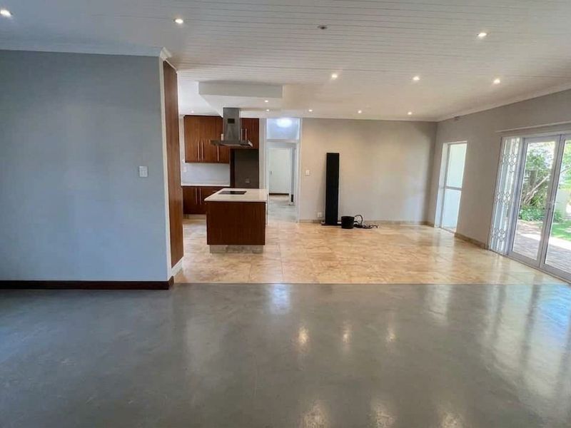 Spacious open-plan living area featuring a modern kitchen with island, polished concrete and tiled flooring, and direct access to the garden through french doors.