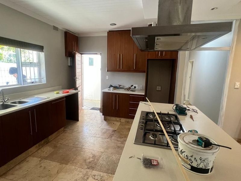 A kitchen space currently undergoing renovation, featuring dark wood cabinetry, stone countertops, a gas hob, and an extractor fan with tiled flooring.