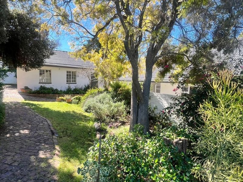 A view of the rear garden featuring a cobblestone pathway leading towards the house with established trees and a tiled roof structure.