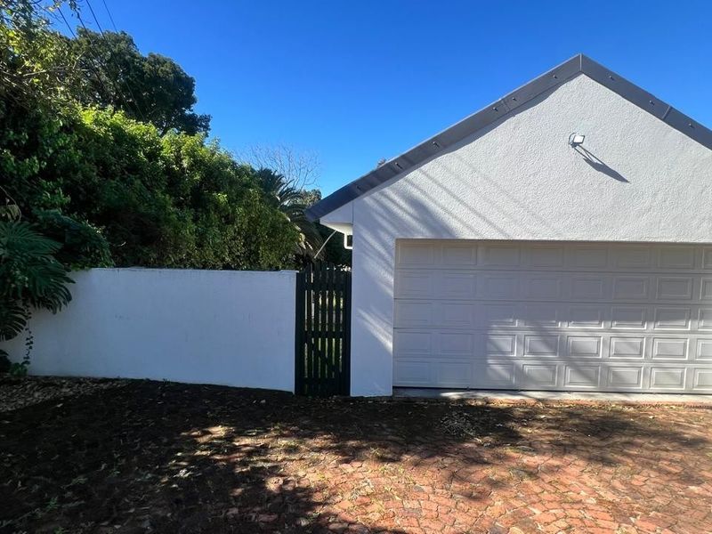 Exterior view of a detached garage featuring a white sectional door, adjacent boundary wall, and a pedestrian gate, set against a paved driveway.