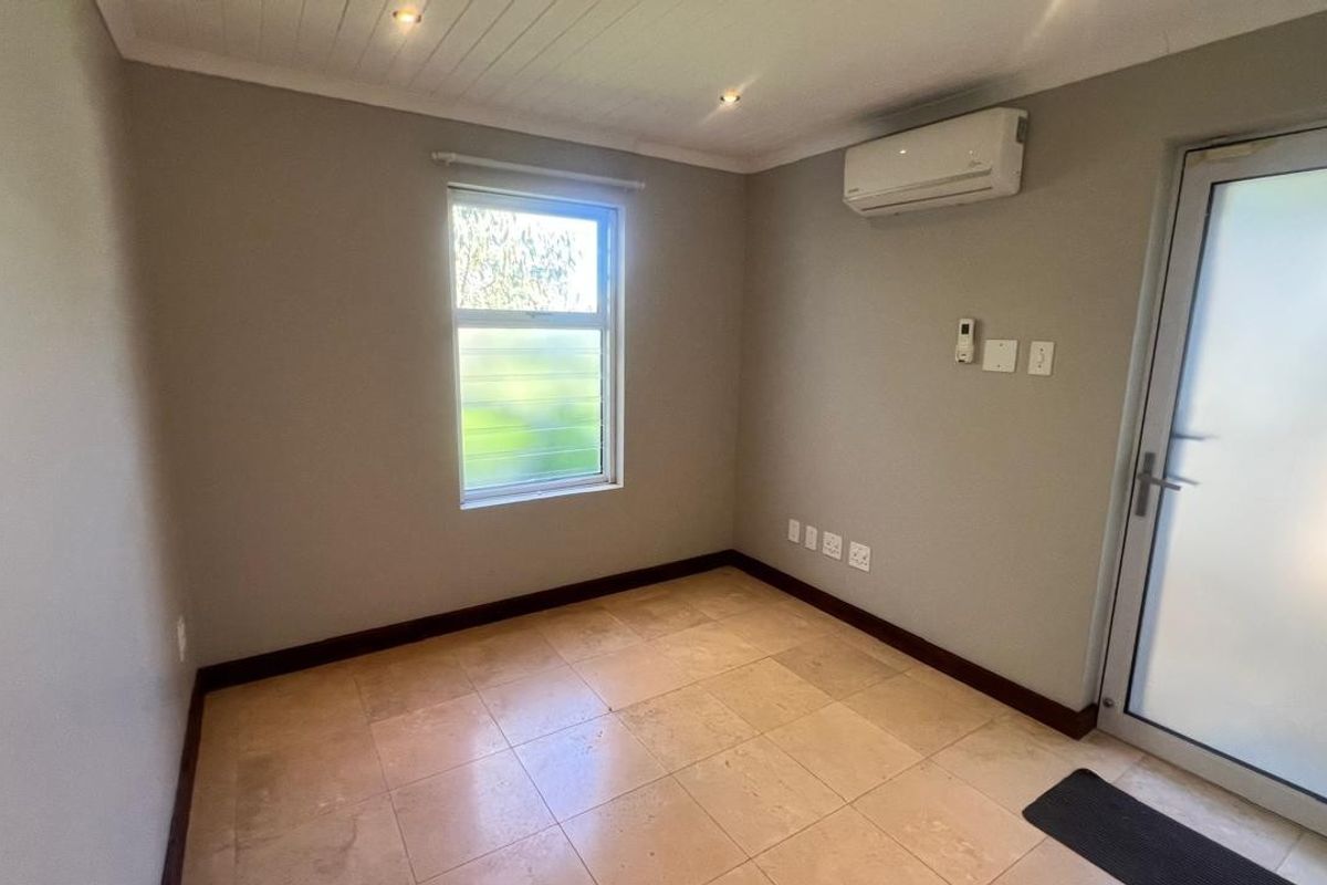 A clean, empty bedroom featuring tiled flooring, a split-system air conditioner, and a frosted glass door leading to the exterior.