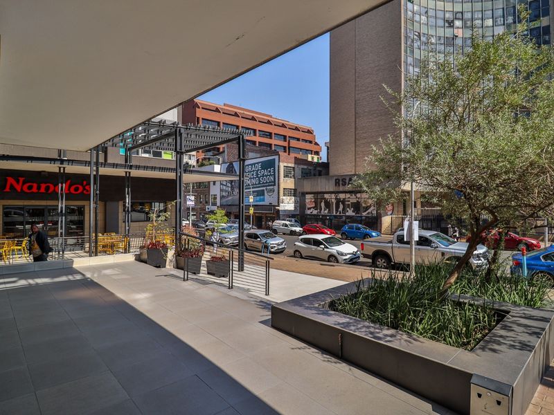 A covered commercial patio area featuring tiled flooring, a raised planter box, and direct access to a street-level storefront.