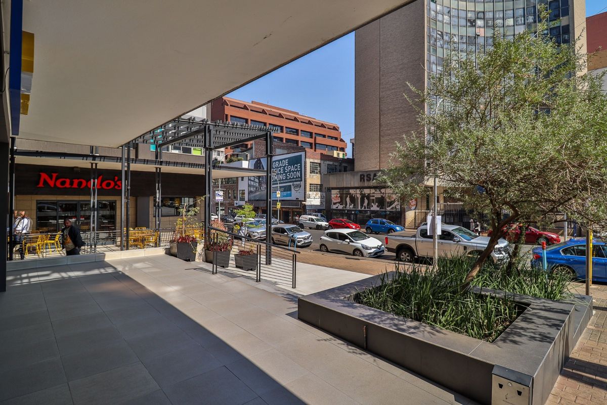A covered commercial patio area featuring tiled flooring, a raised planter box, and direct access to a street-level storefront.