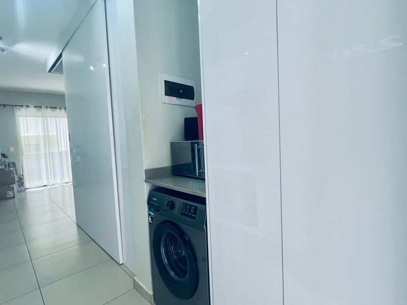 A compact, integrated laundry nook featuring sleek white cabinetry, stone countertop, and dedicated space for a washing machine within the apartment hallway.