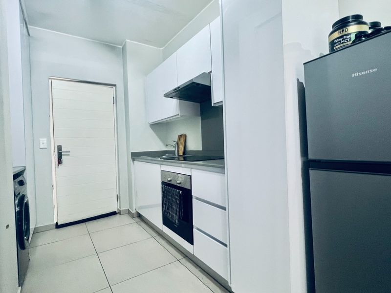 Modern galley-style kitchen featuring white cabinetry, integrated oven and hob, extractor fan, and neutral tiled flooring.