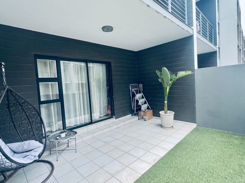A private ground-floor patio featuring tiled flooring, a sliding glass door entrance, and a small section of artificial grass.