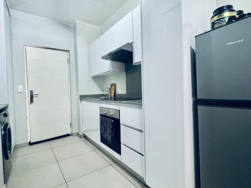 A modern, compact kitchen featuring white cabinetry, integrated oven and hob, extractor fan, and tiled flooring, providing a clean and functional workspace.
