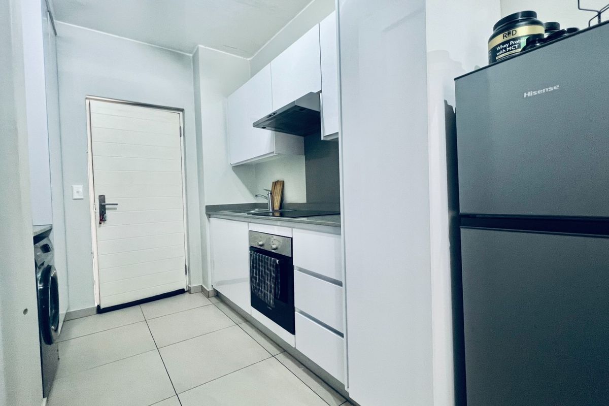 A modern, compact kitchen featuring white cabinetry, integrated oven and hob, extractor fan, and tiled flooring, providing a clean and functional workspace.