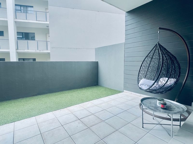 A private balcony featuring tiled flooring, a section of artificial grass, and modern wall cladding, providing a compact outdoor living space.