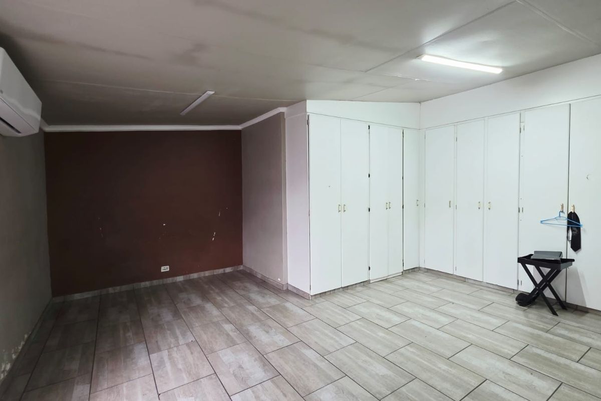 A spacious bedroom featuring neutral tiled flooring, extensive built-in cupboard storage, and a wall-mounted air conditioning unit.