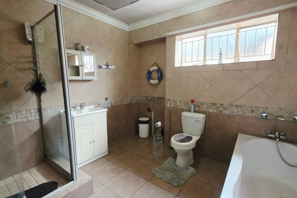 A functional bathroom featuring a glass shower enclosure, a separate bathtub, a vanity cabinet with basin, and tiled finishes throughout.
