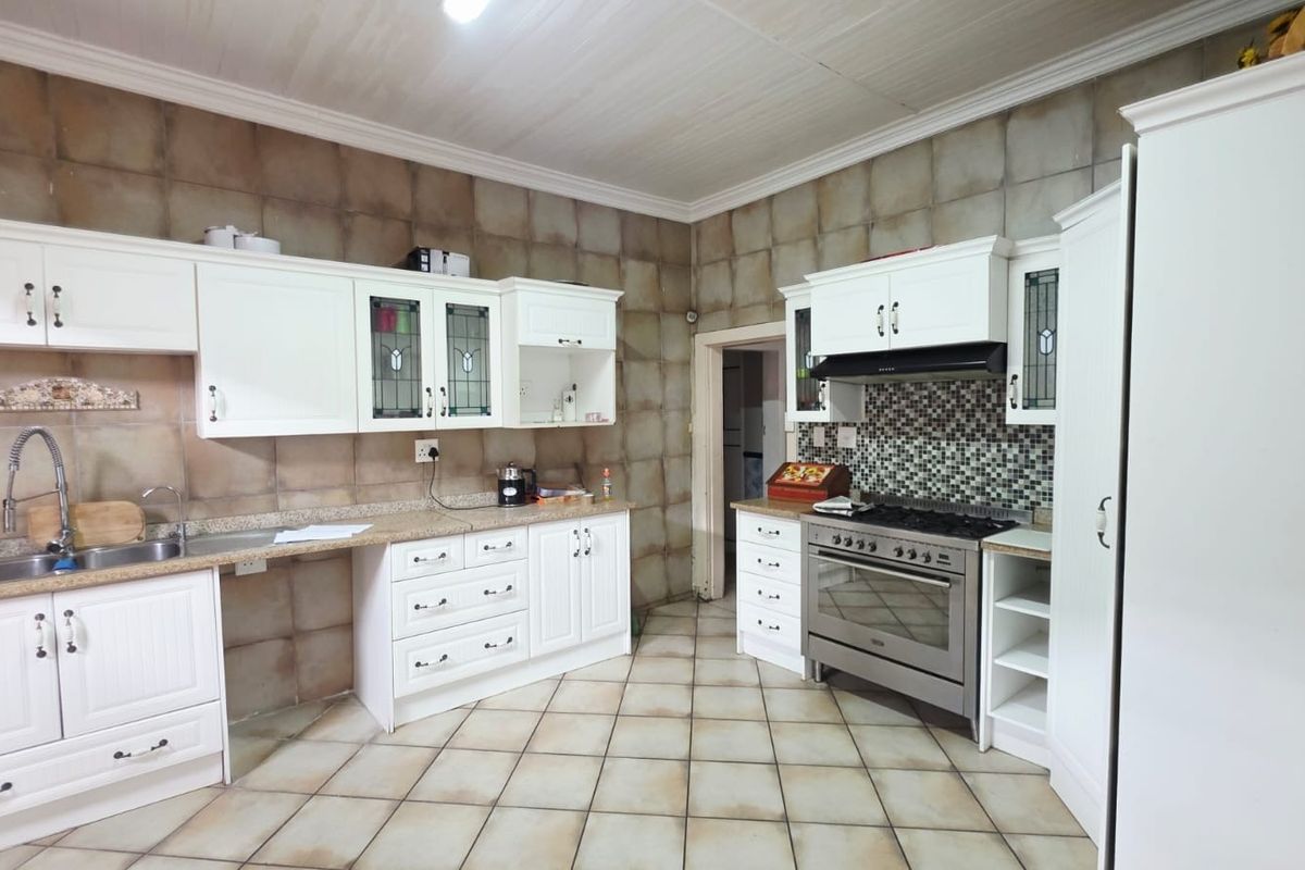 A functional kitchen featuring white cabinetry, granite countertops, a gas stove with extractor fan, and tiled wall and floor finishes.
