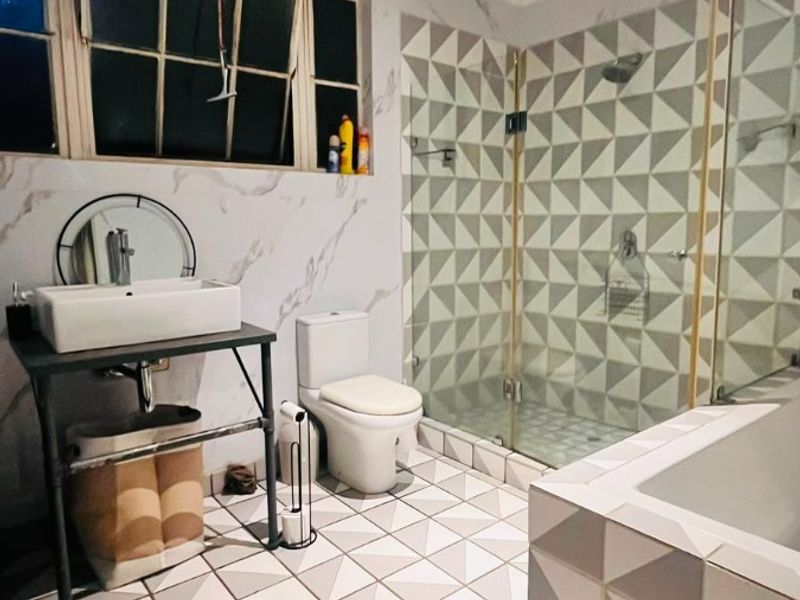 Modern bathroom featuring a vessel sink, glass-enclosed shower, built-in bathtub, and striking geometric tile work on both the floors and shower walls.