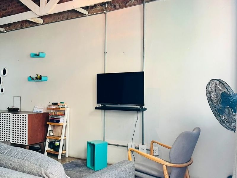 Industrial-style living room featuring exposed brick walls, timber roof trusses, and polished concrete floors with exposed conduit electrical detailing.