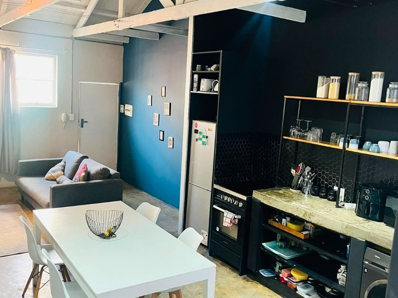 Open-plan living and kitchen area featuring industrial-style exposed timber roof trusses, polished concrete flooring, and a modern kitchen with concrete countertops.