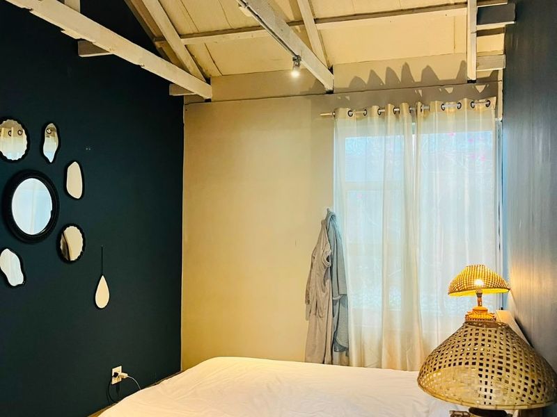 A bedroom featuring high ceilings with exposed timber roof trusses, polished concrete flooring, and modern track lighting.