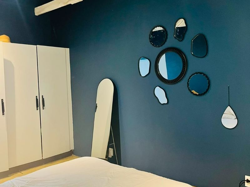 A bedroom featuring dark blue walls, exposed white roof trusses, built-in wardrobe storage, and polished concrete flooring.