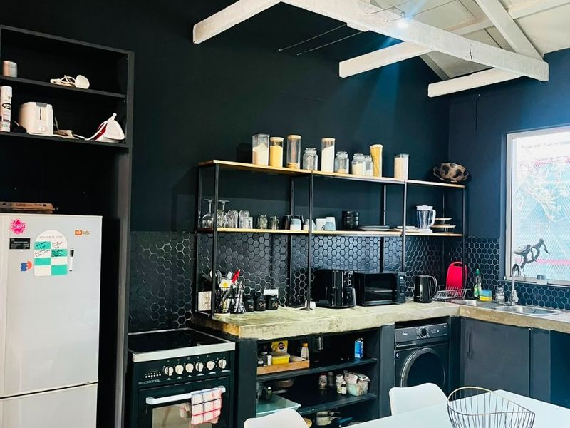 Modern kitchen featuring exposed white timber rafters, dark cabinetry, hexagonal tile backsplash, and concrete countertops with integrated shelving and built-in oven.