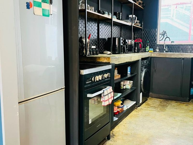 Industrial-style kitchen featuring black cabinetry, hexagonal tile backsplash, concrete countertops, open shelving, and integrated appliances with polished concrete flooring.
