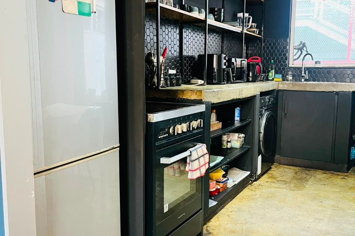 Industrial-style kitchen featuring black cabinetry, hexagonal tile backsplash, concrete countertops, open shelving, and integrated appliances with polished concrete flooring.