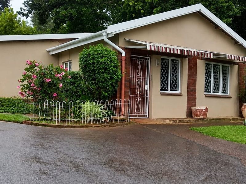 Front elevation of the property featuring a paved driveway, security gate entrance, and protective window bars.