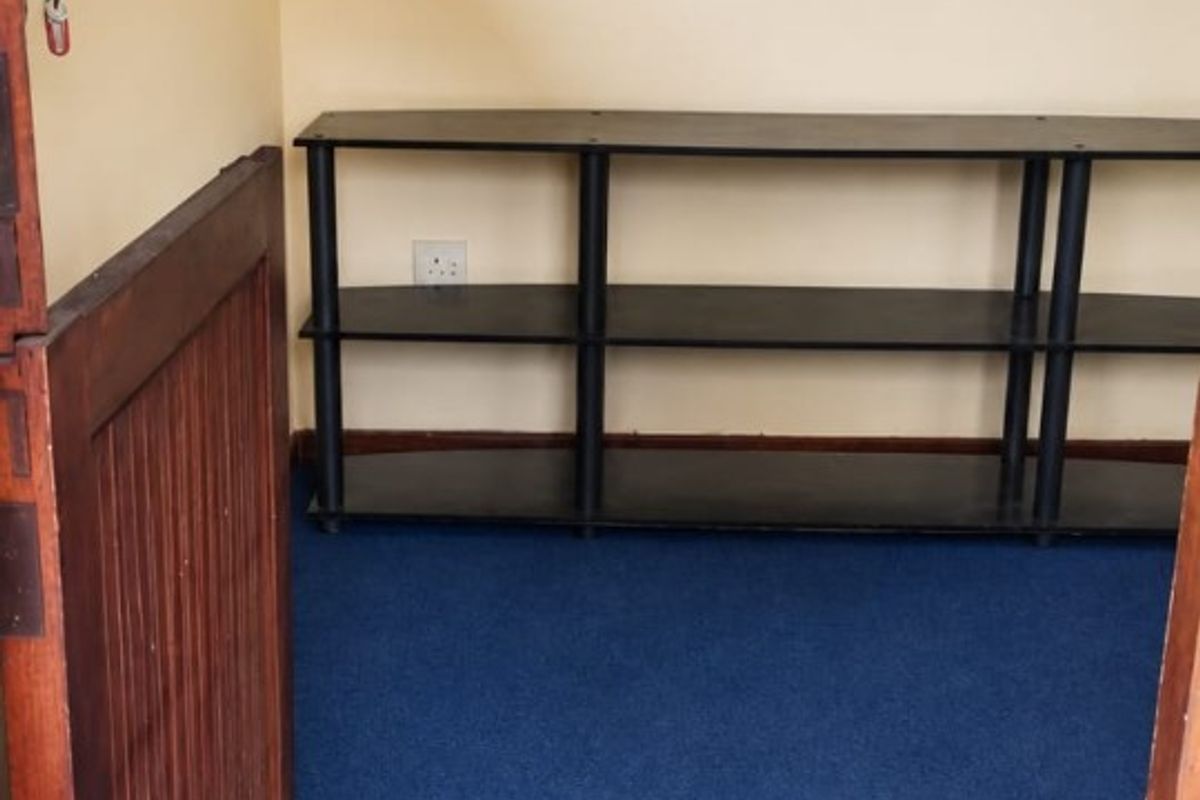 A small, empty bedroom featuring blue carpeting, a window with security bars, and a neutral wall finish, ready for renovation or staging.