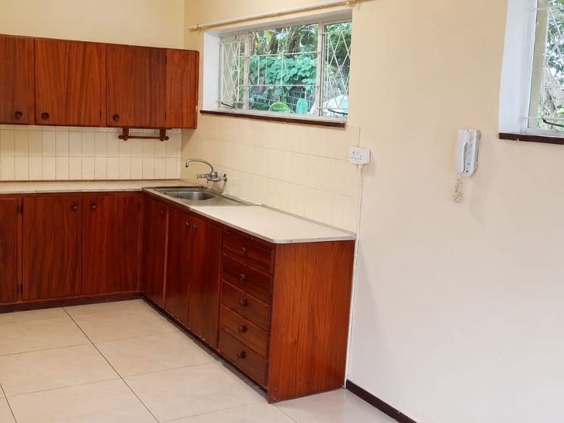 A functional kitchen featuring traditional wooden cabinetry, tiled backsplash, and ample counter space with a stainless steel sink and security-fitted windows.