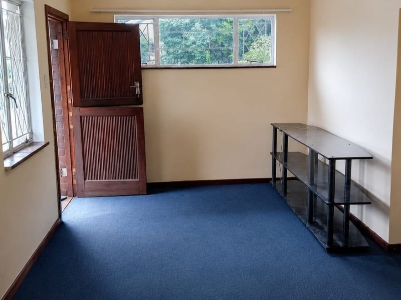 An empty living area featuring blue carpeting, a traditional stable-style wooden door, and security bars on the windows.