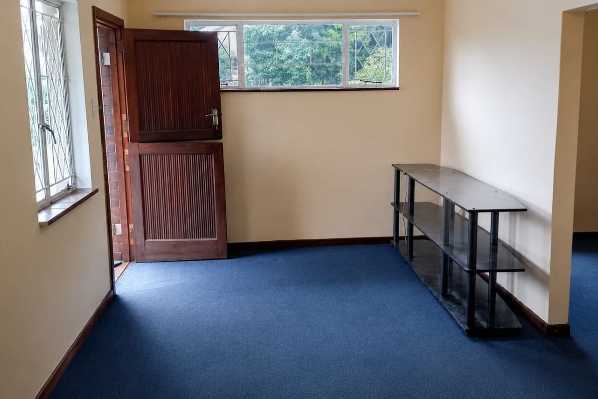 An empty living area featuring blue carpeting, a traditional stable-style wooden door, and security bars on the windows.