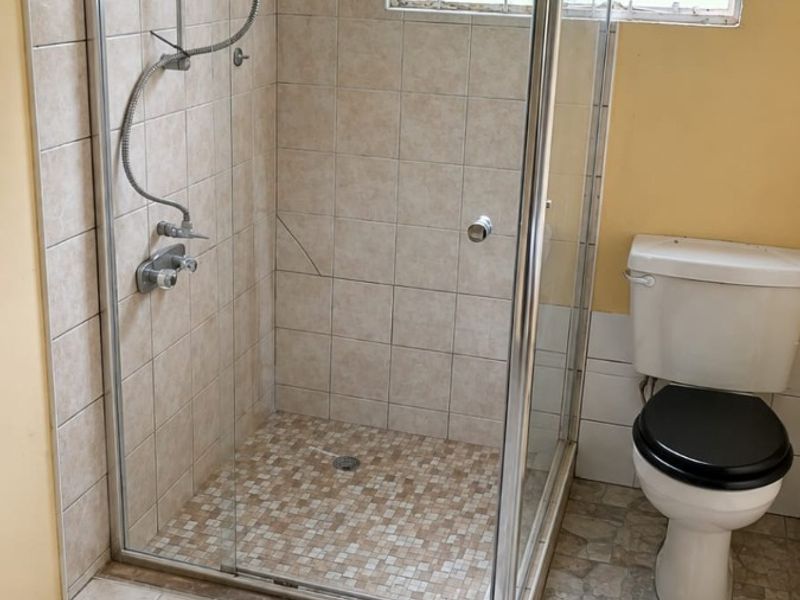 A functional bathroom featuring a glass-enclosed shower, tiled flooring, and a standard toilet, ready for modernization and cosmetic updates.