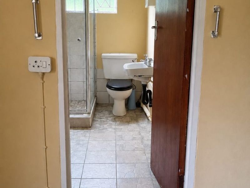 A functional bathroom featuring a shower enclosure, pedestal basin, and toilet, with tiled flooring and dated finishes throughout.
