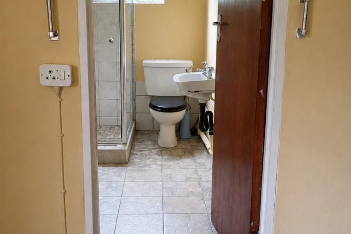 A functional bathroom featuring a shower enclosure, pedestal basin, and toilet, with tiled flooring and dated finishes throughout.