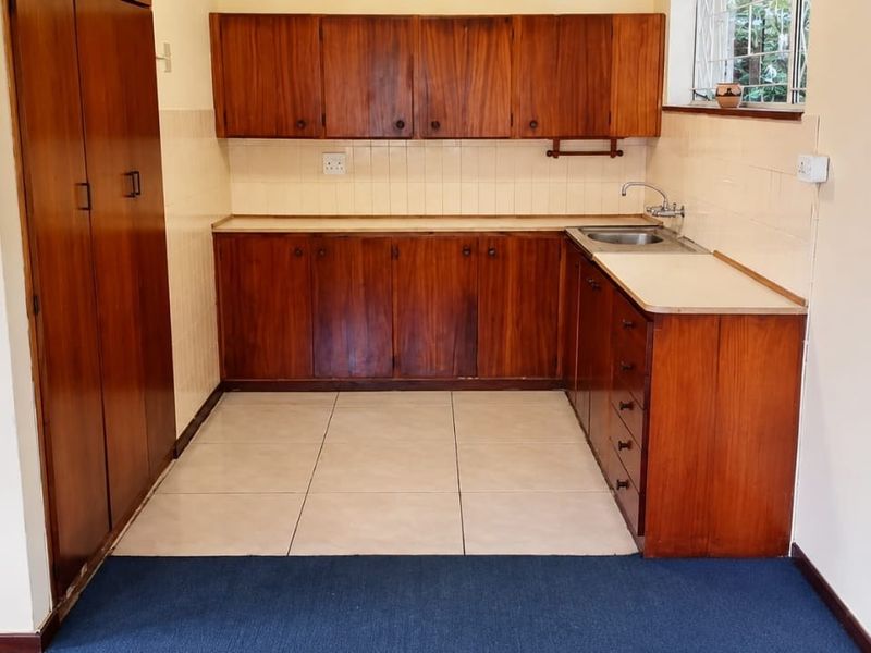 A functional kitchen featuring wooden cabinetry, laminate countertops, a stainless steel sink, and tiled flooring, offering a clean space ready for modernization.