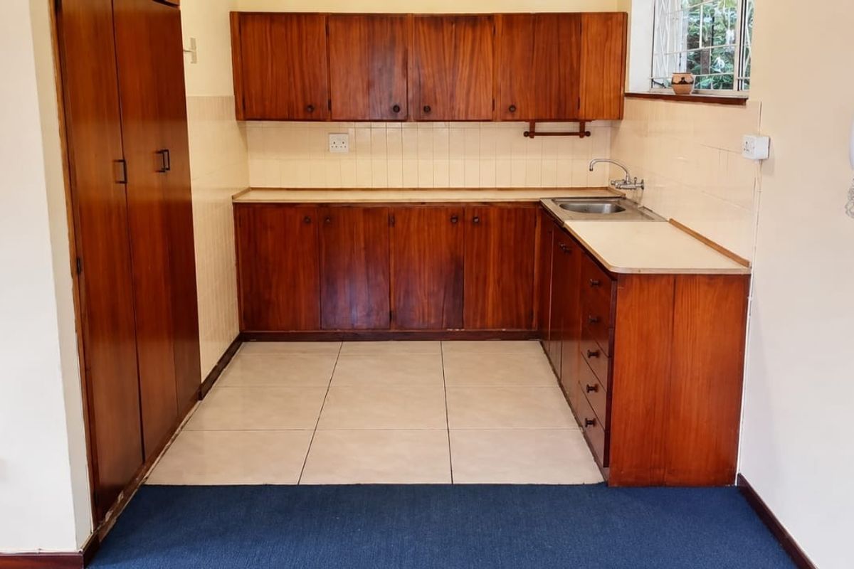A functional kitchen featuring wooden cabinetry, laminate countertops, a stainless steel sink, and tiled flooring, offering a clean space ready for modernization.