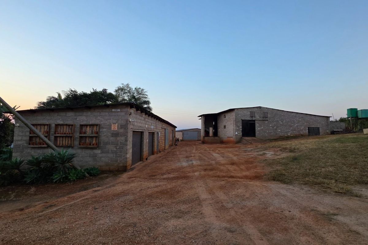 View of farm outbuildings featuring cinder block construction, roller shutter doors, and corrugated metal roofing, situated along a dirt access path.
