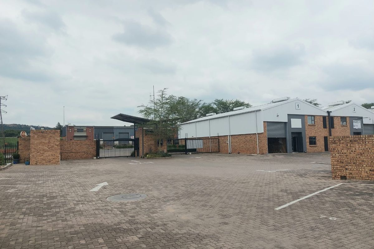 Industrial property exterior featuring a paved driveway, brick facade, and secure roller shutter access points.