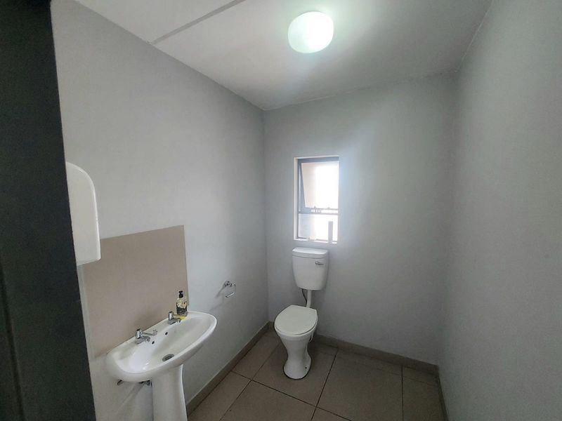 A functional, minimalist bathroom featuring a pedestal washbasin, a standard toilet, and tiled flooring with neutral wall finishes.