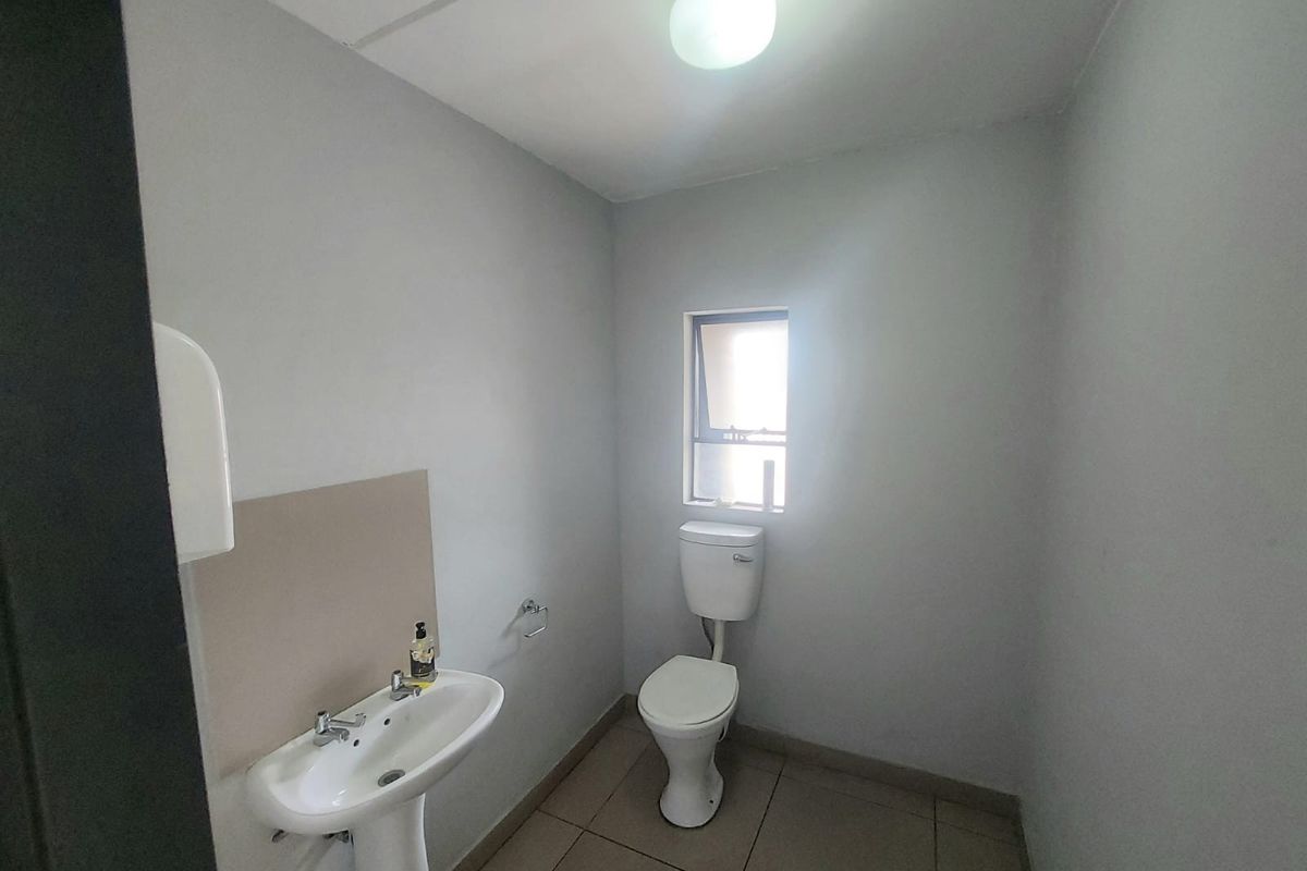 A functional, minimalist bathroom featuring a pedestal washbasin, a standard toilet, and tiled flooring with neutral wall finishes.