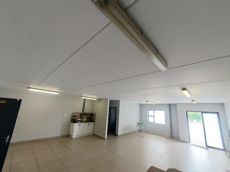 Spacious open-plan industrial unit featuring tiled flooring, built-in kitchenette cabinetry, and ample natural light through a sliding glass door.