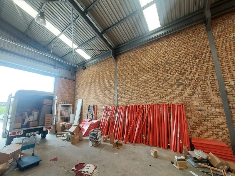 Spacious industrial warehouse unit featuring high ceilings with exposed steel trusses, natural light from skylights, facebrick walls, and a large roller shutter door.