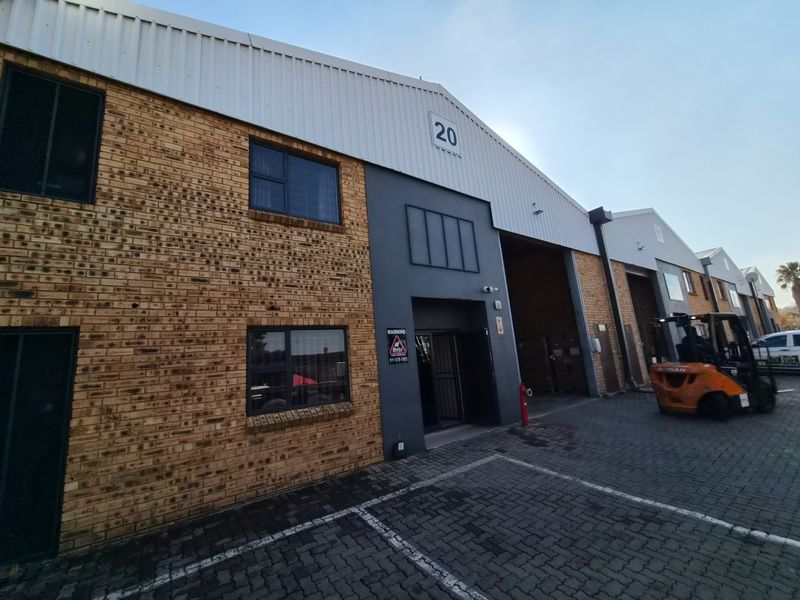 Front elevation of an industrial warehouse unit featuring face brick and metal cladding, with a paved driveway and secure entrance.