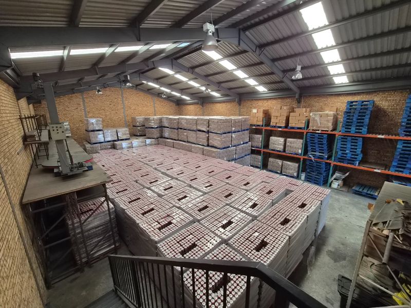 Spacious industrial warehouse featuring exposed steel roof trusses, skylights, face brick walls, and heavy-duty metal racking systems for efficient storage and logistics operations.