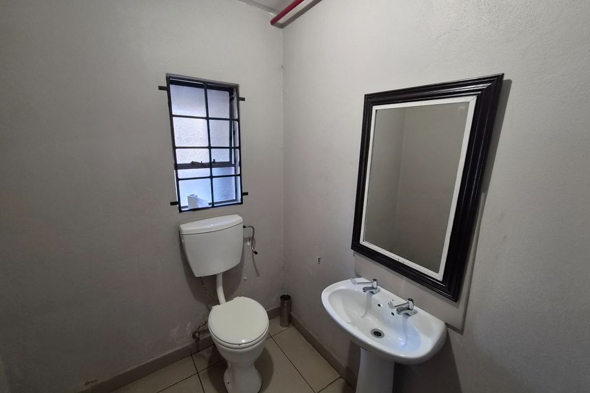 A functional industrial-style bathroom featuring a pedestal basin, toilet, and security-barred window, requiring minor cosmetic updates to improve its overall appearance.