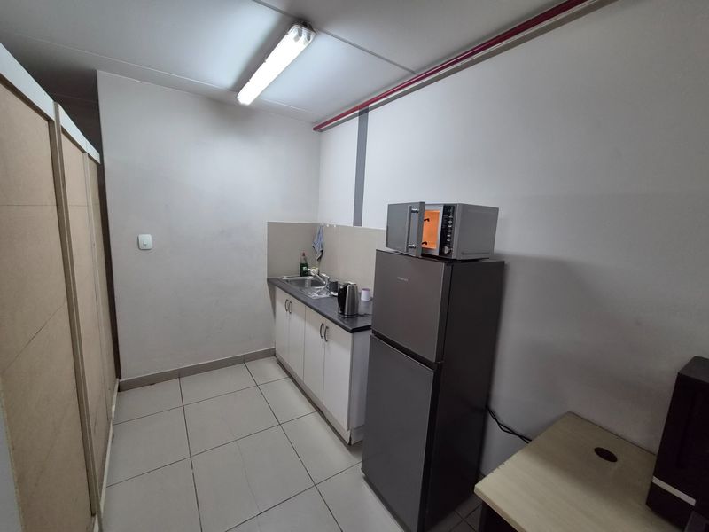 A functional kitchenette area featuring built-in cabinetry, a stainless steel sink, and tiled flooring, suitable for office or industrial utility use.